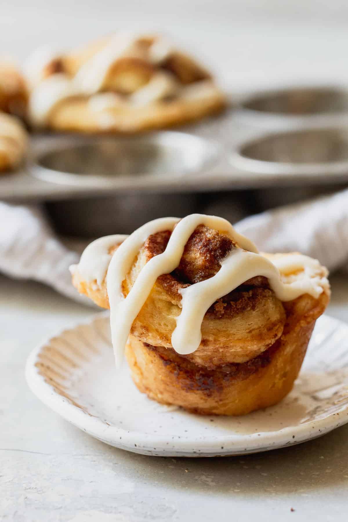 A single cinnamon roll biscuit on a white plate with cinnamon biscuits in the background