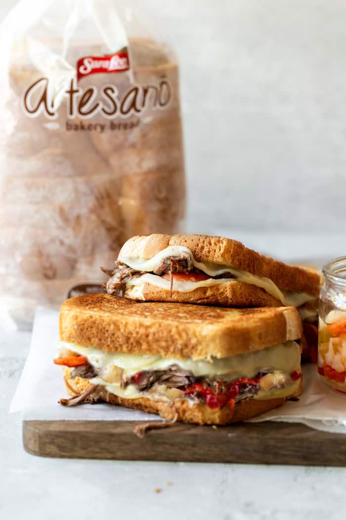 A close up of two Italian beef grilled cheeses with bread in the background