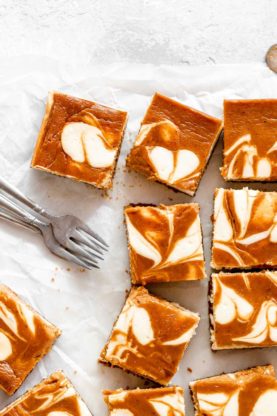 Swirled cheesecake bars with pumpkin scattered against parchment paper