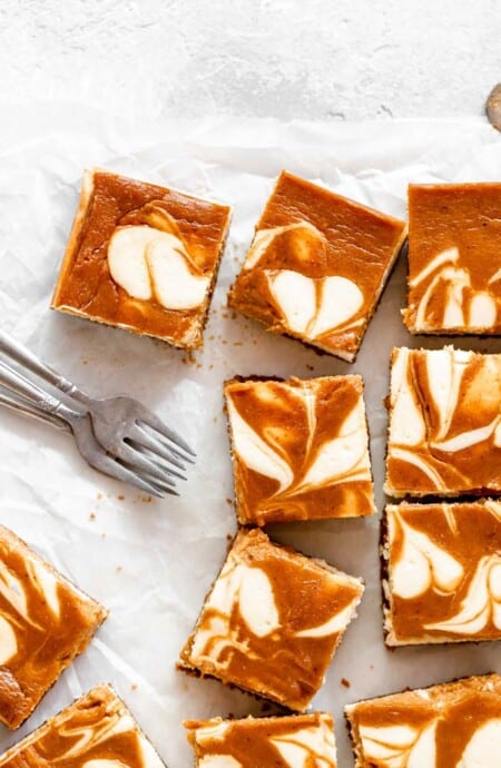 Swirled cheesecake bars with pumpkin scattered against parchment paper