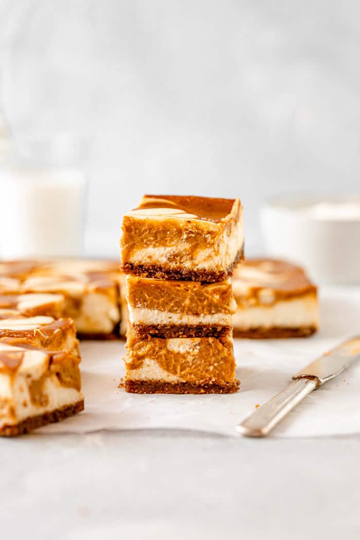 Pumpkin cheesecake bars stacked on top of each other with a large knife and bars behind it