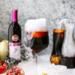 A delicious sangria recipe in a wine glass with dry ice next to a full carafe