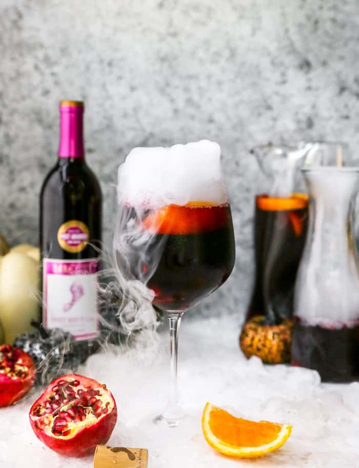 A delicious sangria recipe in a wine glass with dry ice next to a full carafe
