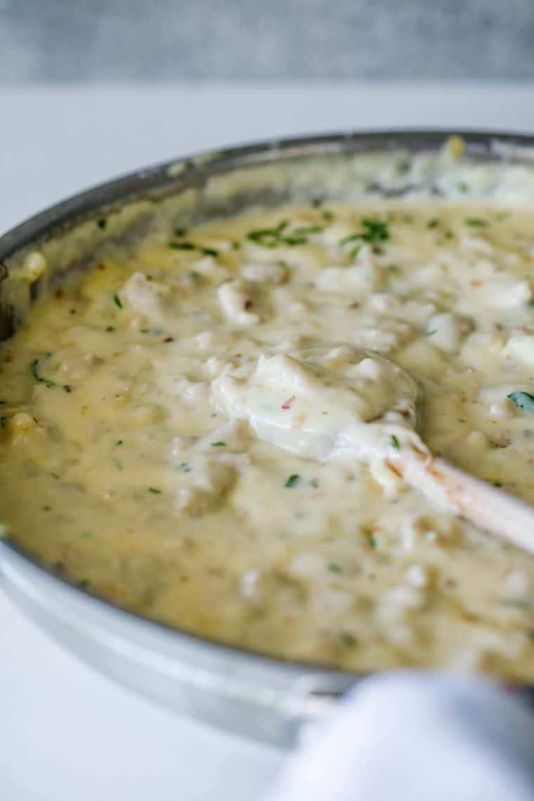 A pan filled with white sausage gravy with a wooden spoon sharing this