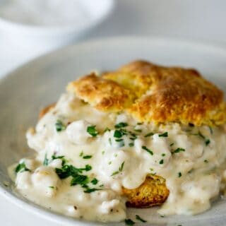 A buttermilk biscuit filled with white sausage gravy on a white plate