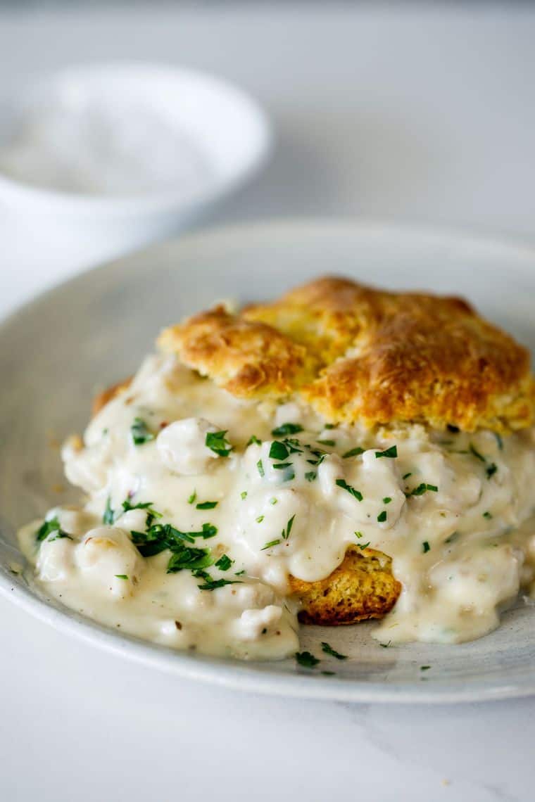 A buttermilk biscuit filled with white sausage gravy on a white plate