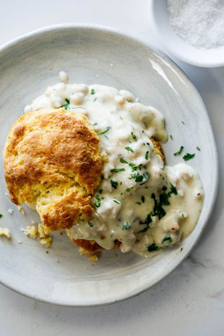 A buttermilk biscuit filled with sawmill gravy spilling over on a white plate
