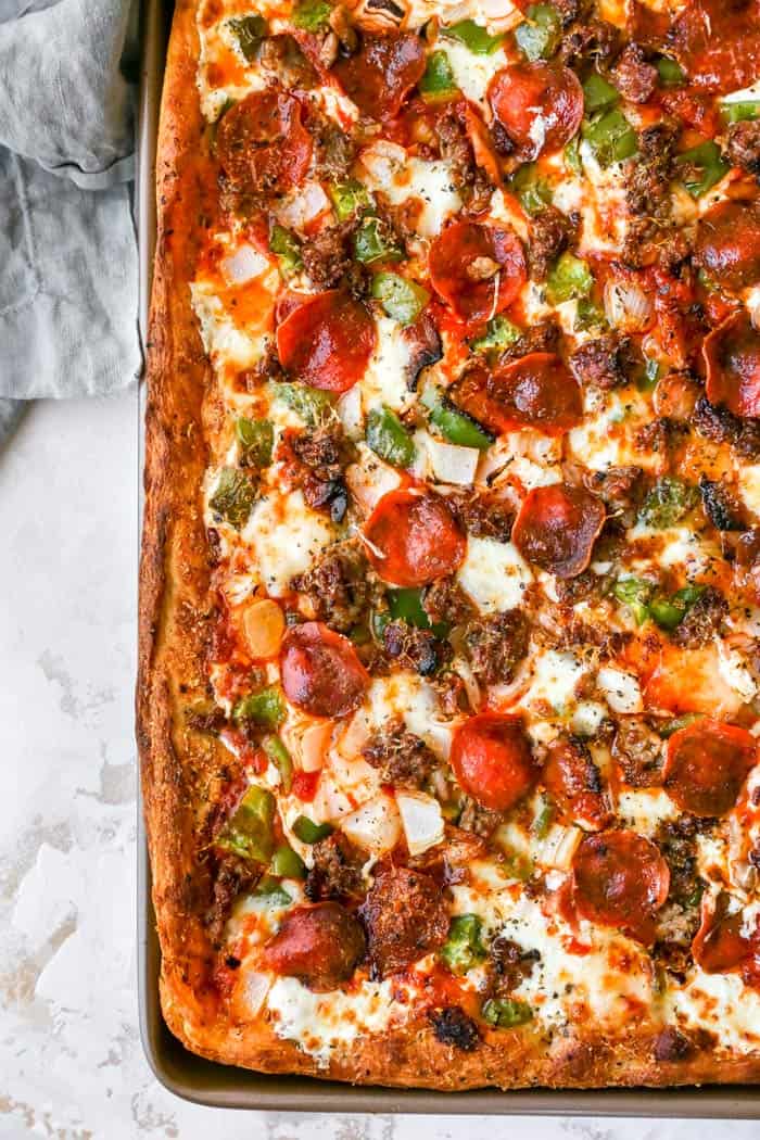 An overhead of a full sheet of deep dish pizza with pepperoni and sausage and peppers