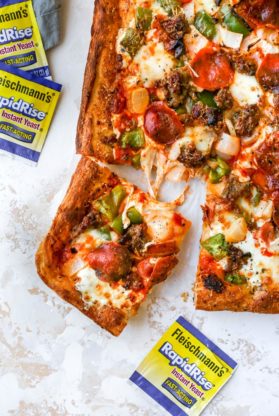 A large sicilian pizza with a slice cut next to packets of instant yeast