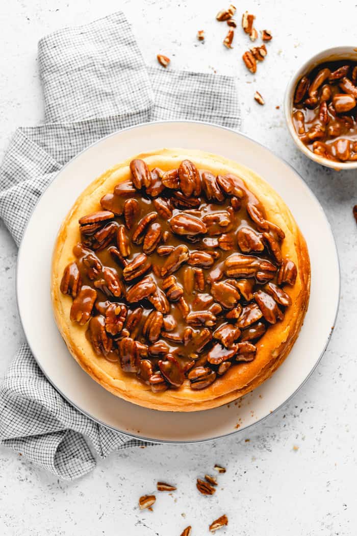 An overhead of a perfectly baked butter pecan cheesecake with a bowl of pecans nearby