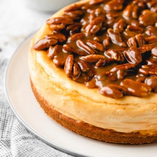 A close up of pecan cheesecake with a caramel topping on a white plate