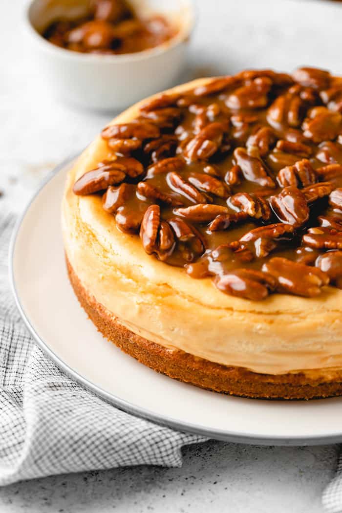 A close up of pecan cheesecake with a caramel topping on a white plate
