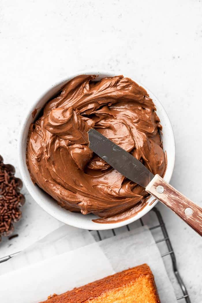 A bowl of perfectly whipped chocolate swiss meringue buttercream with sprinkles nearby and a spatula