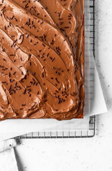 The corner of a sheet cake topped with chocolate swiss meringue buttercream and chocolate sprinkles