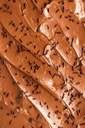 A close up of a chocolate buttercream topped sheet cake and chocolate sprinkles