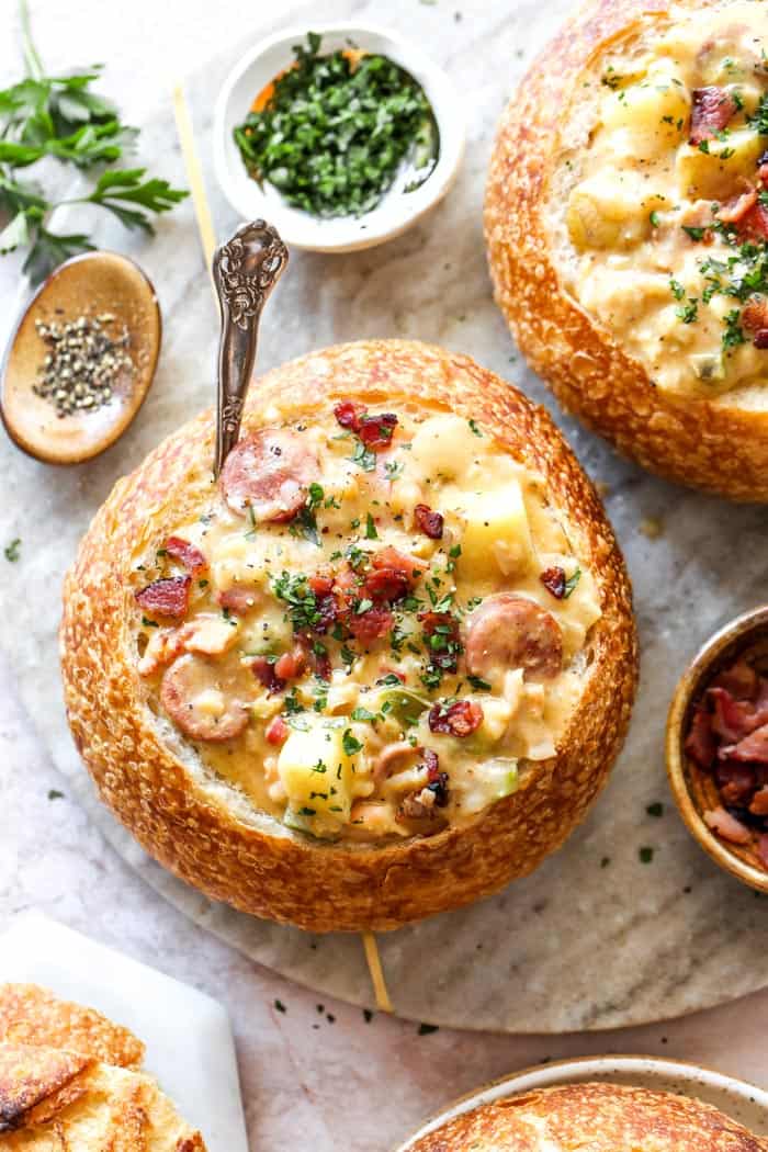 Two bread bowls filled with cajun clam chowder with bacon bits and parsley sprinkled on top