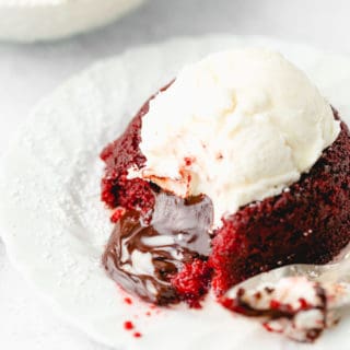 A close up of red velvet lava cake with inside spilling out and vanilla ice cream melting over it