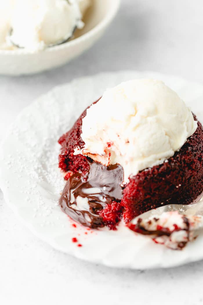 A close up of red velvet lava cake with inside spilling out and vanilla ice cream melting over it