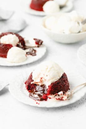 Two red velvet molten lava cakes on white plates topped with vanilla ice cream melting down