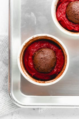 A close up of a ramekin filled with red velvet cake batter with a ball of chocolate on top