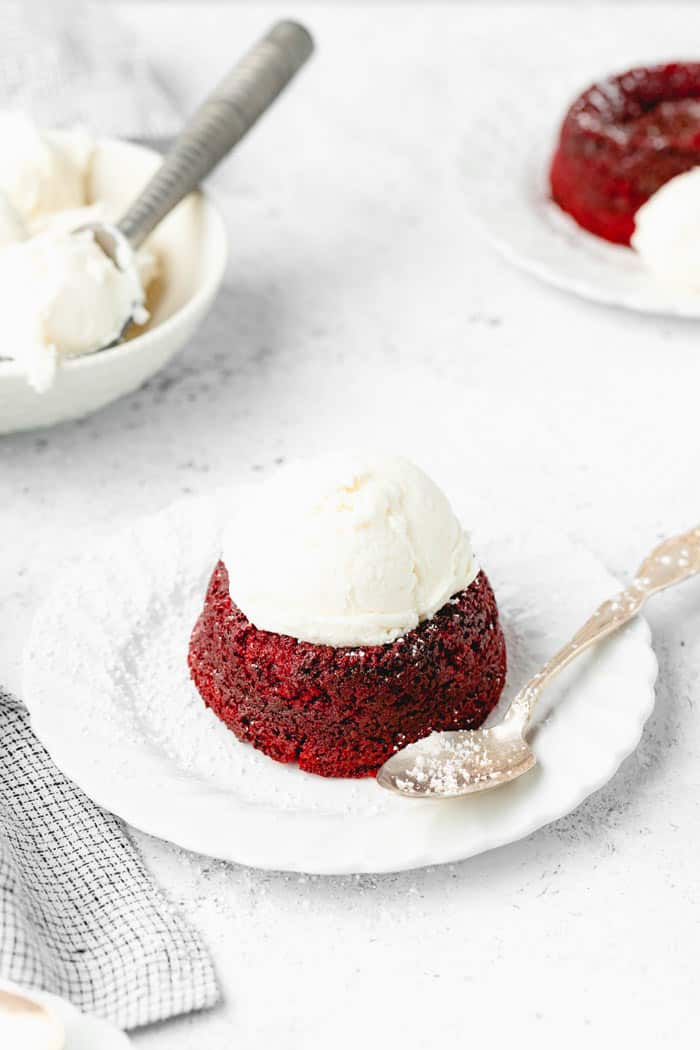 A red velvet lava cake on a white vintage plate with a spoon topped with vanilla ice cream