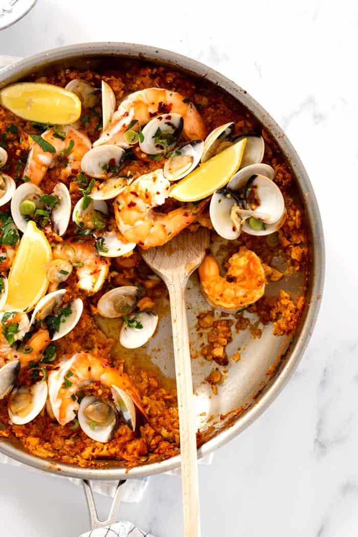 An overhead of a seafood paella in a silver skillet with a wooden spoon serving