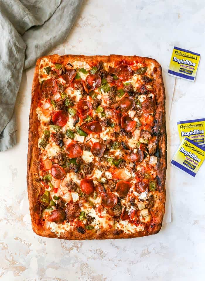 An overhead of a full sheet of deep dish pizza with pepperoni and sausage and peppers