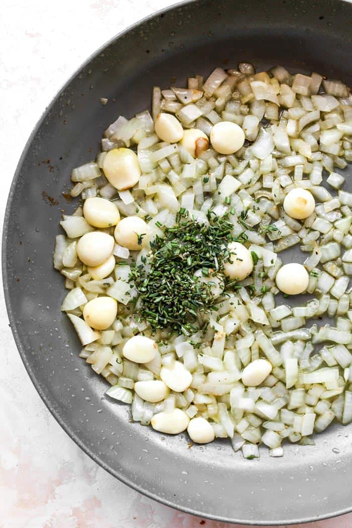 garlic cloves and herbs sauteeing in a pan