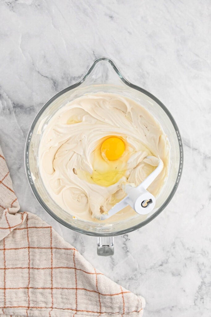 Butter pecan cheesecake batter in mixer with egg being added