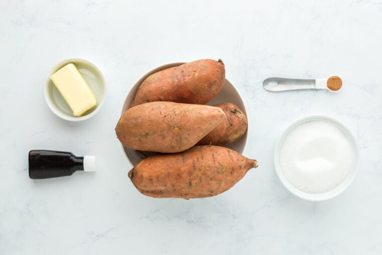 Sweet potatoes, nutmeg, butter, granulated sugar and vanilla on a white countertop