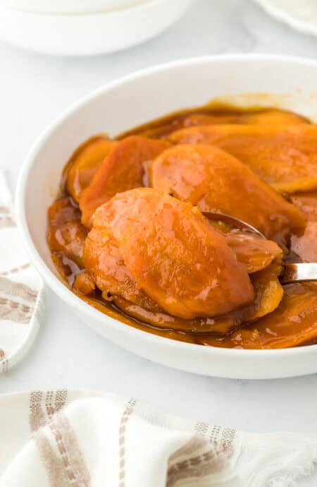 Sliced candy sweet potatoes being lifted fro white bowl ready to enjoy