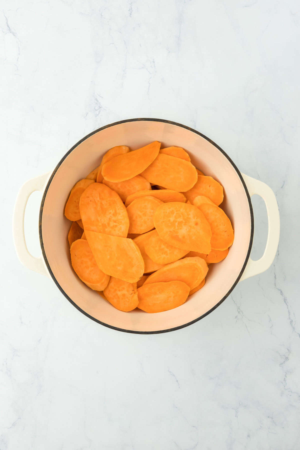 Sliced sweet potatoes in a large white pot on white countertop