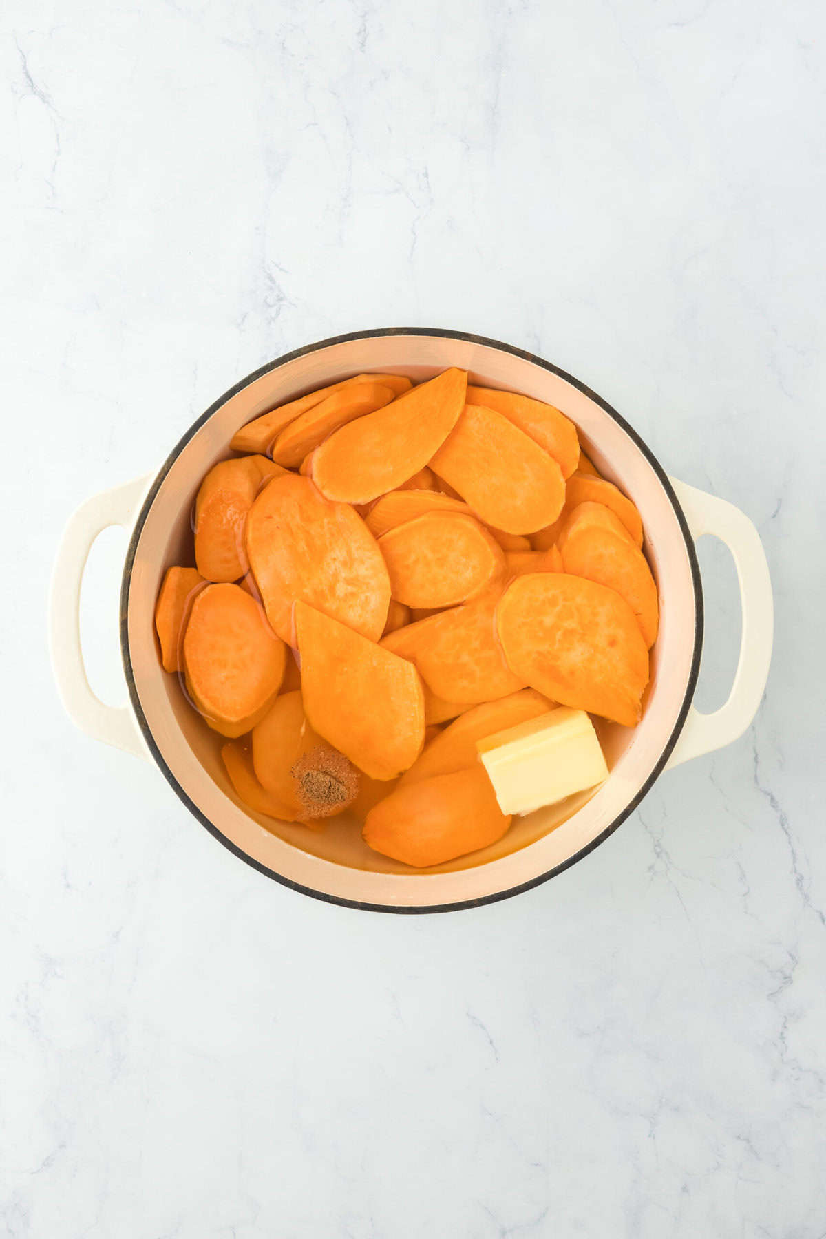 Water, butter, and spices added to a pot with sliced sweet potatoes