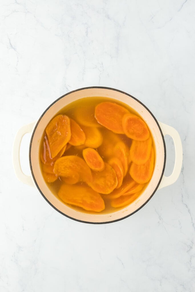Tender sweet potato slices in water in large pot on white countertop.
