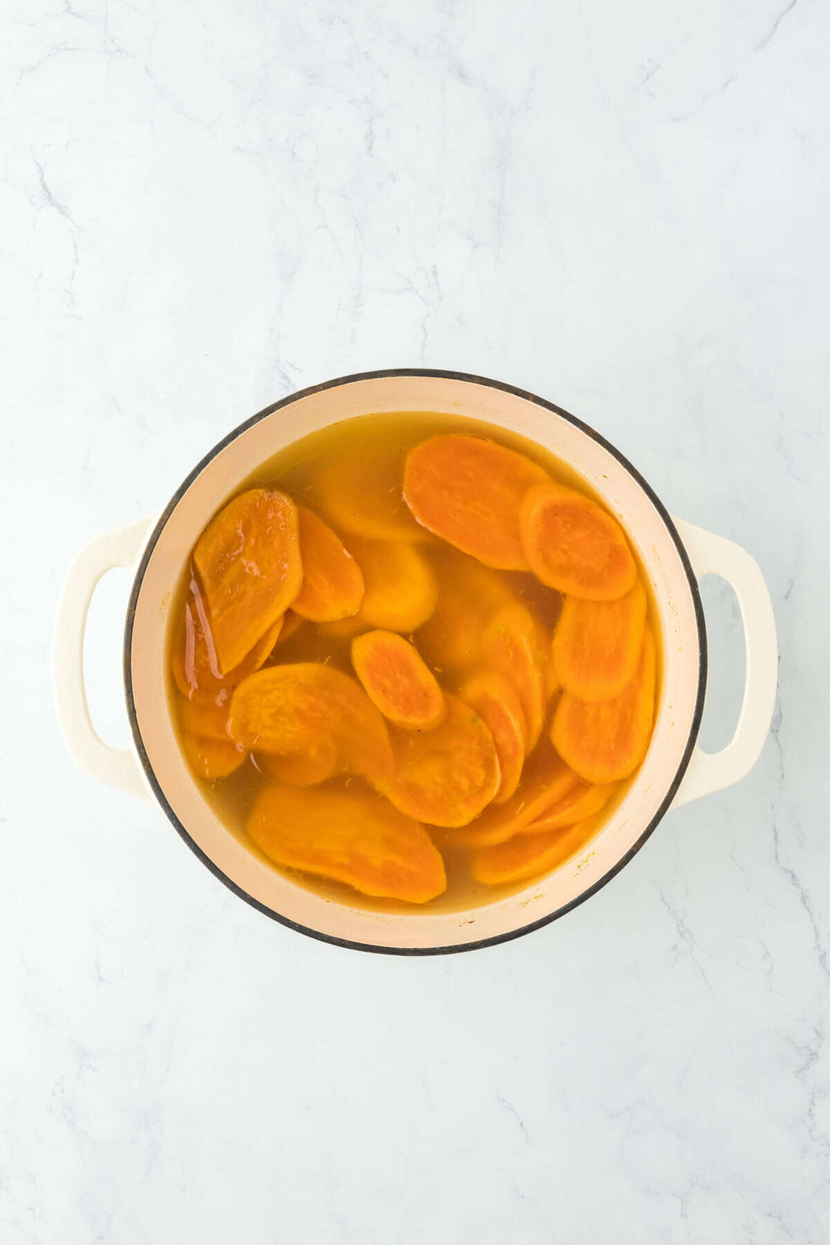 Tender sweet potato slices in water in large pot on white countertop.