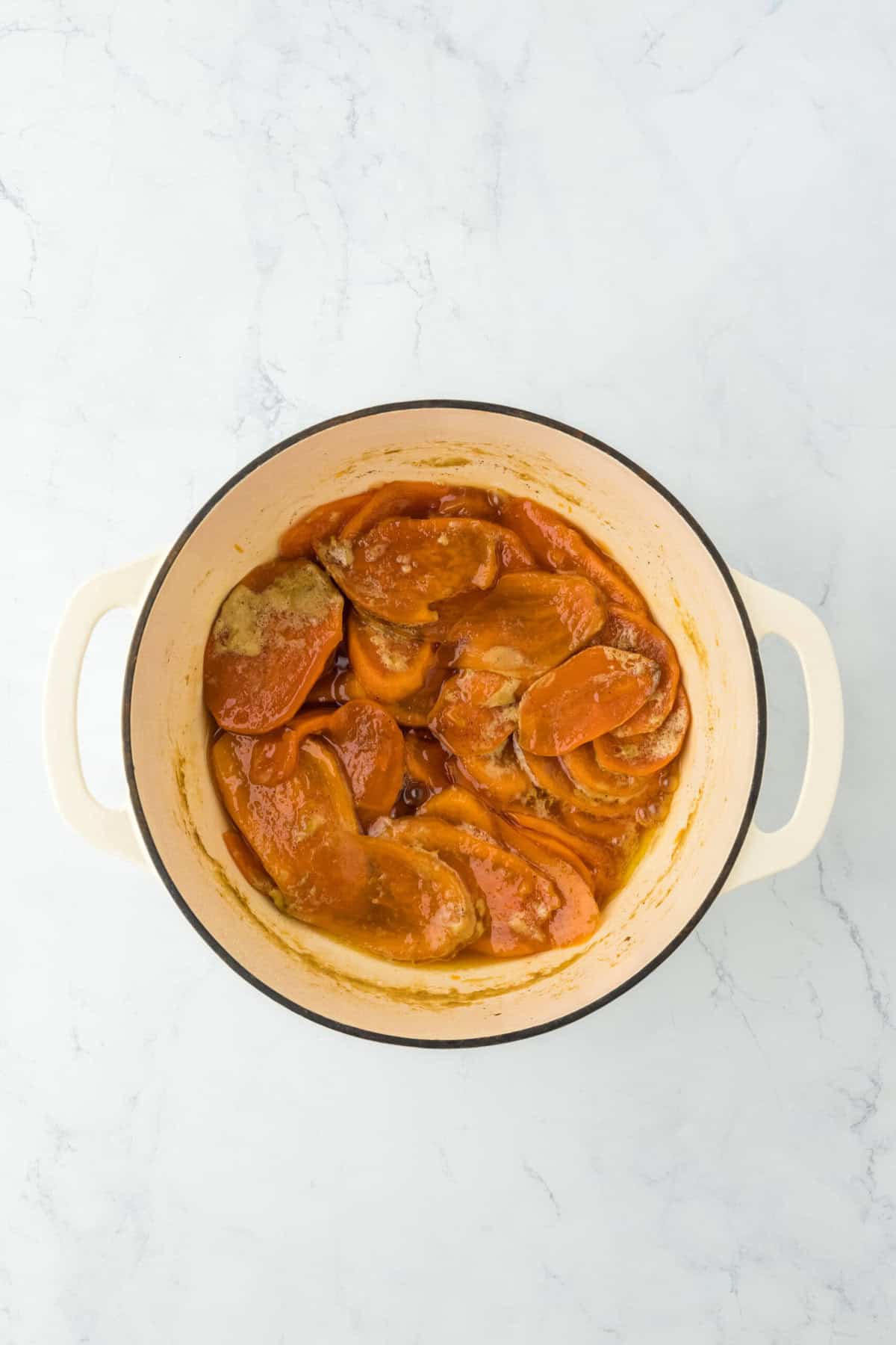 Stove top candied sweet potatoes after being cooked in a white pot on white countertop