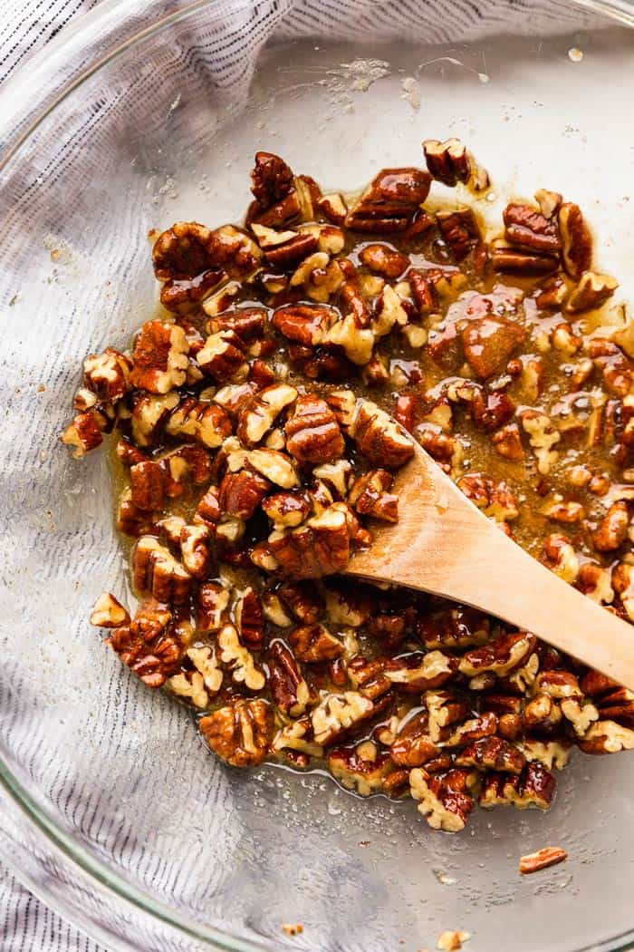 A pecan pie filling in a clear bowl with wooden spoon