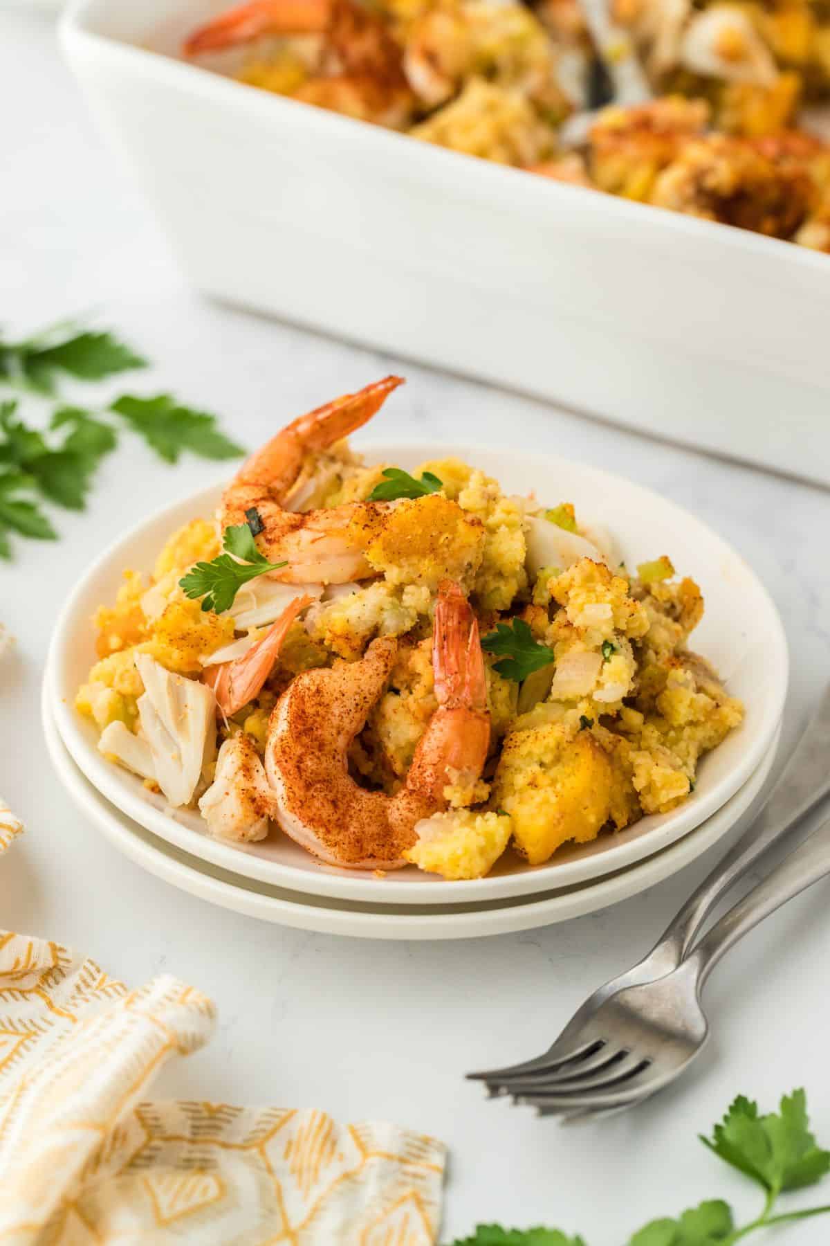 A serving of seafood dressing on a plate, surrounded by fresh parsley, with the baking dish slightly visible in the background