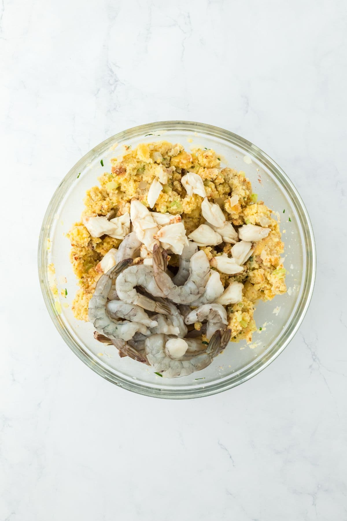 A glass bowl containing raw shrimp and lump crab added to the dressing mix