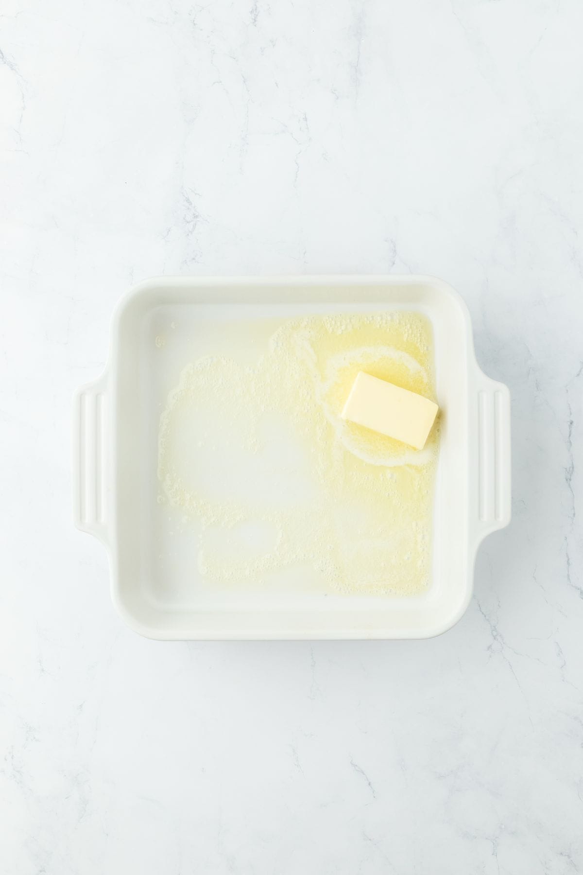 A white baking dish with butter melting in the bottom