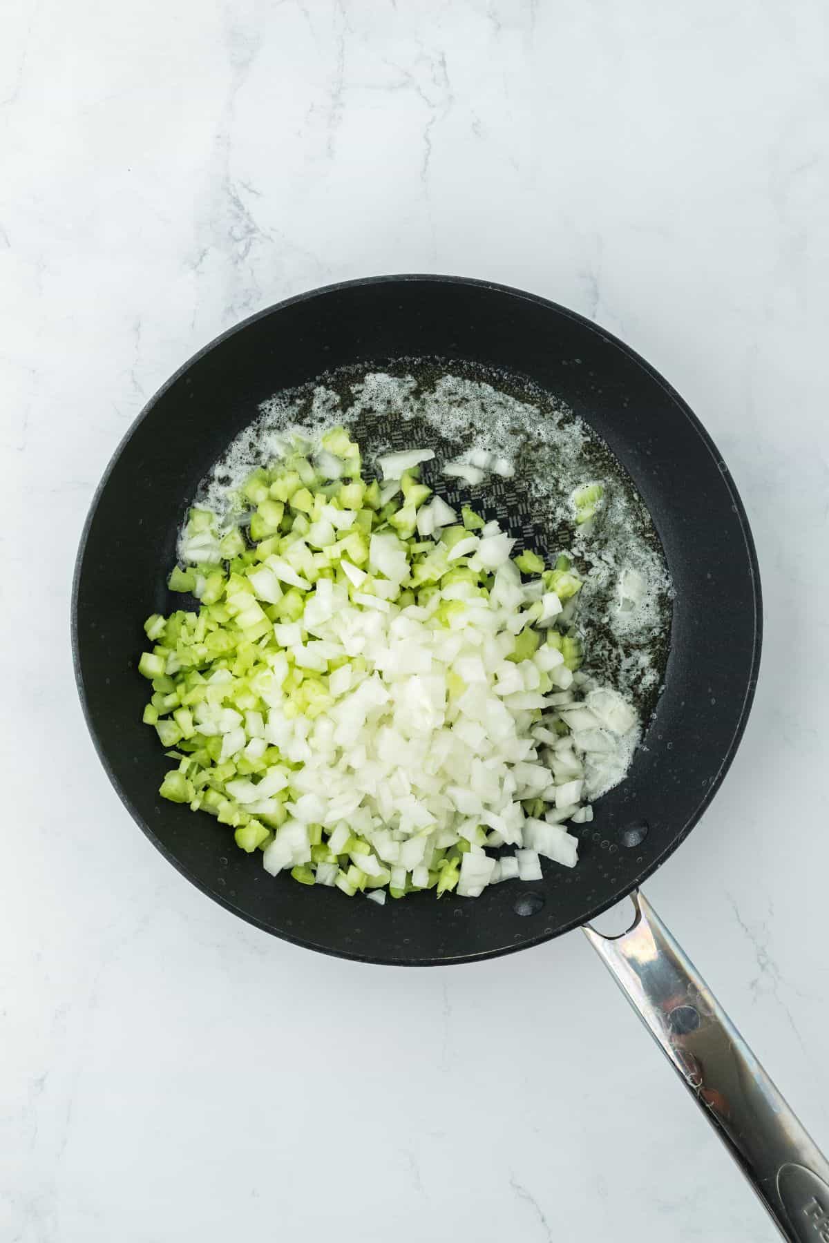 A skillet filled with chopped onions and celery being sautéed