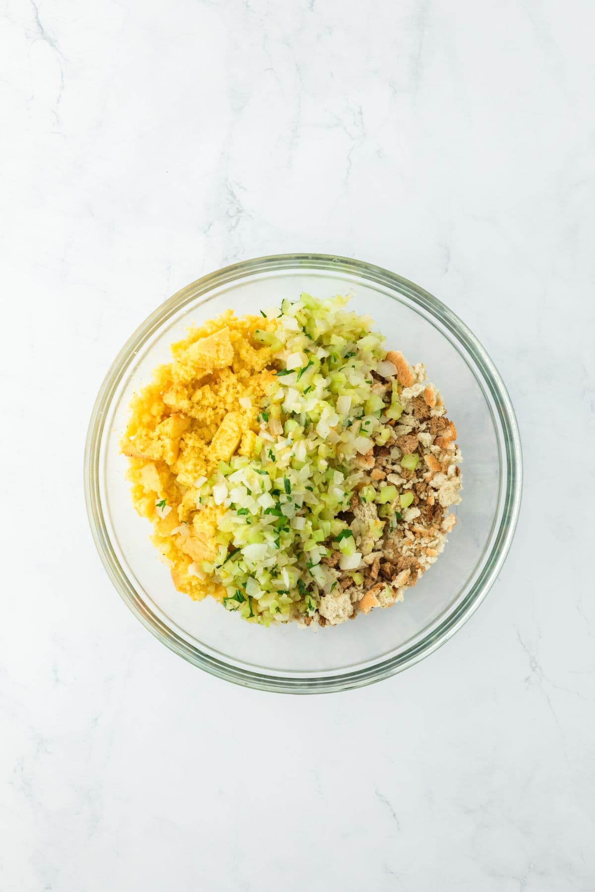 A mixing bowl containing cornbread, crumbled bread, and cooked vegetables, ready to be mixed