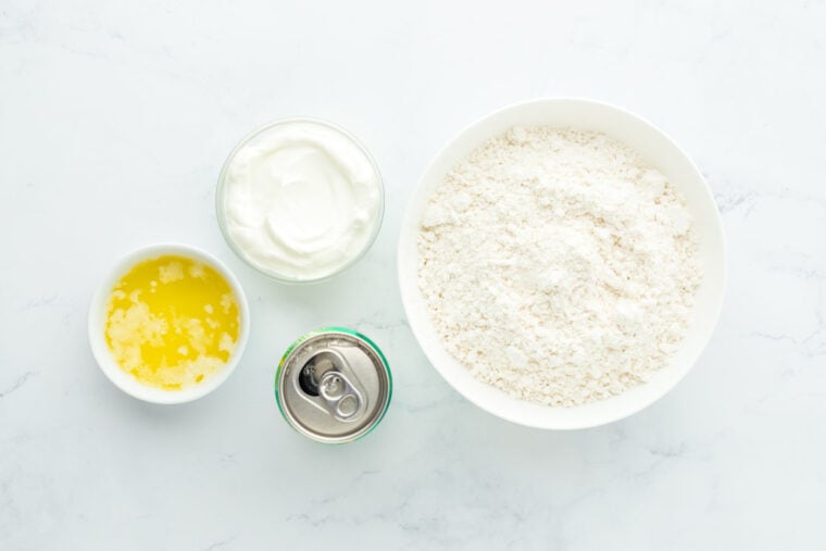 Flour mixture, butter, 7 up and sour cream in white bowls on white countertop