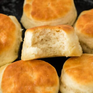 7up biscuits in a cast iron skillet with one having a bite in it.