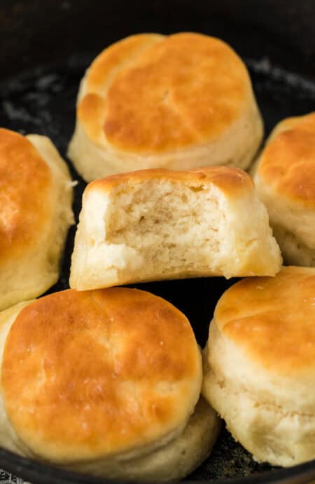 7up biscuits in a cast iron skillet with one having a bite in it.