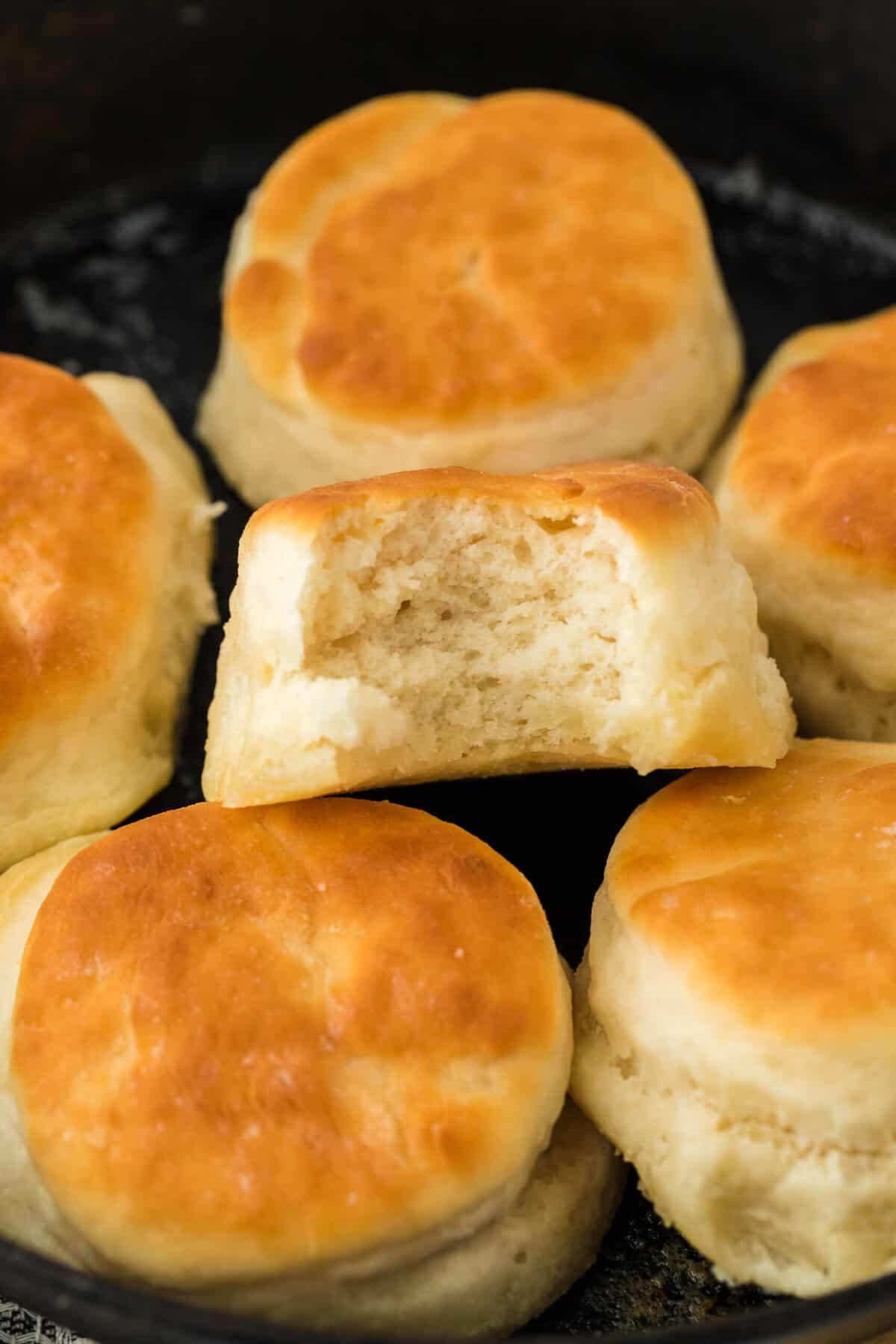 7up biscuits in a cast iron skillet with one having a bite in it.