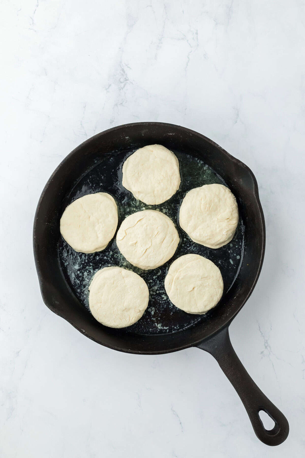 Biscuit dough cut in rounds in cast iron skillet in melted butter