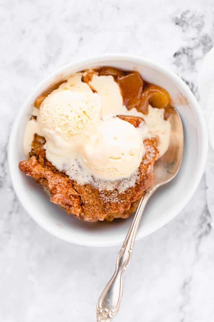 Vanilla ice cream melting down over a biscuit topped cobbler with apples with a gold spoon ready to eat