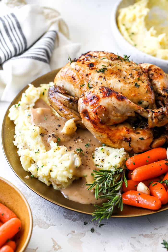 A cornish hen served over mashed potatoes, gravy, and carrots against a white background