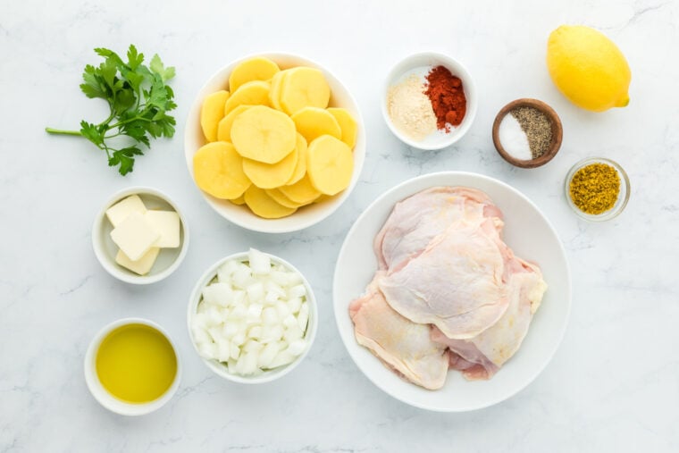 Chicken, sliced potatoes, spices, lemon, onion, on white countertop